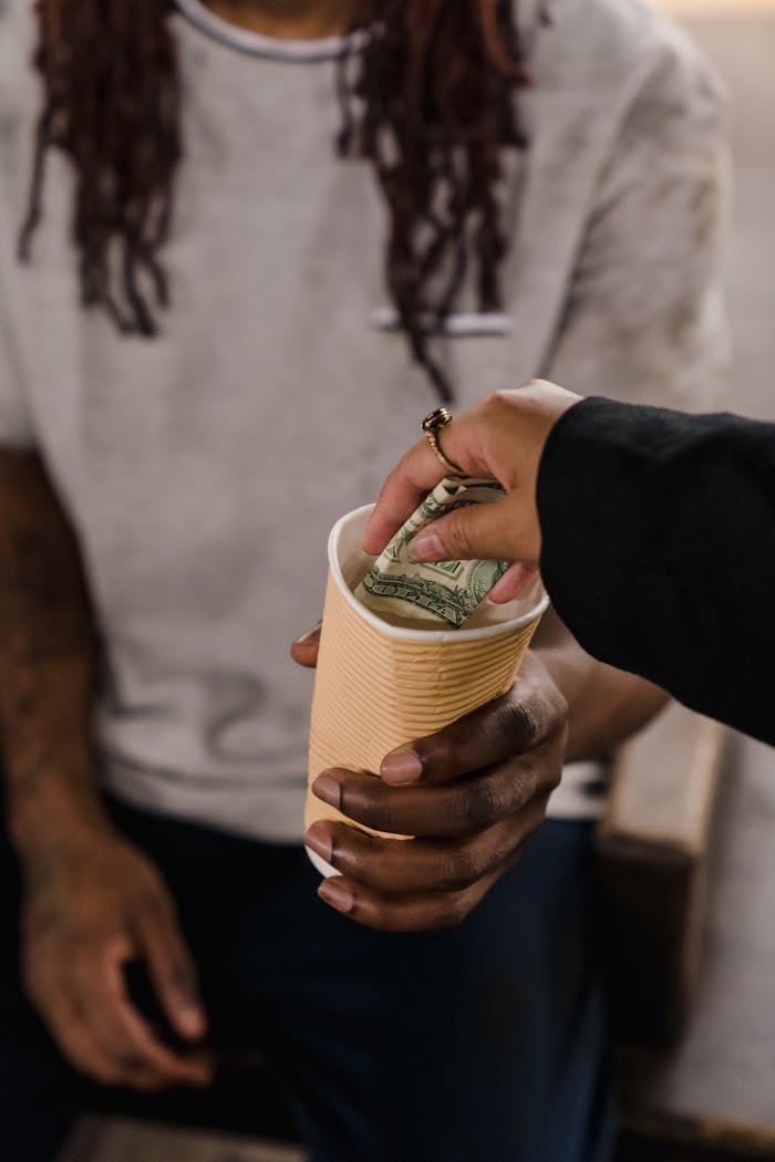 A hand giving money to a person holding a cup, reflecting generosity and support.